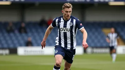 A focused ST Johnstone midfielder in a navy blue and white striped kit, sprinting with the ball at his feet during a...