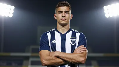 A 26-year-old left-back in a navy blue and white striped football kit, standing confidently with arms crossed
