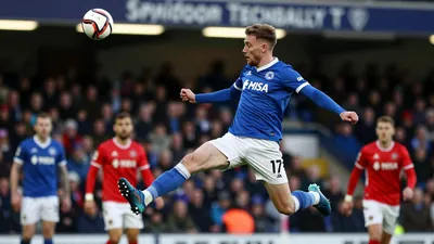 A tight action shot of a St Johnstone player, wearing a blue jersey with a white collar, and white shorts, with a blue...