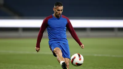 Mid-30s forward, athletic build, waist-up, eyes focused, right foot mid-kick, ball blurred just beyond his boot, wearing...