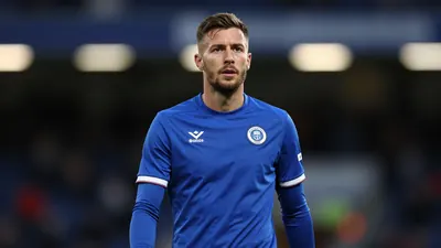 A mid-30s anonymous St Johnstone midfielder in a solid blue kit, waist-up, focused expression, background blurred stadium...